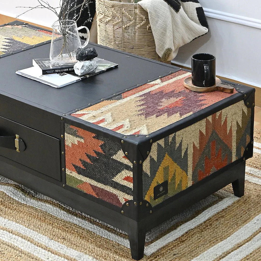 Coffee table with black finish and patterned fabric top in a living room setting.